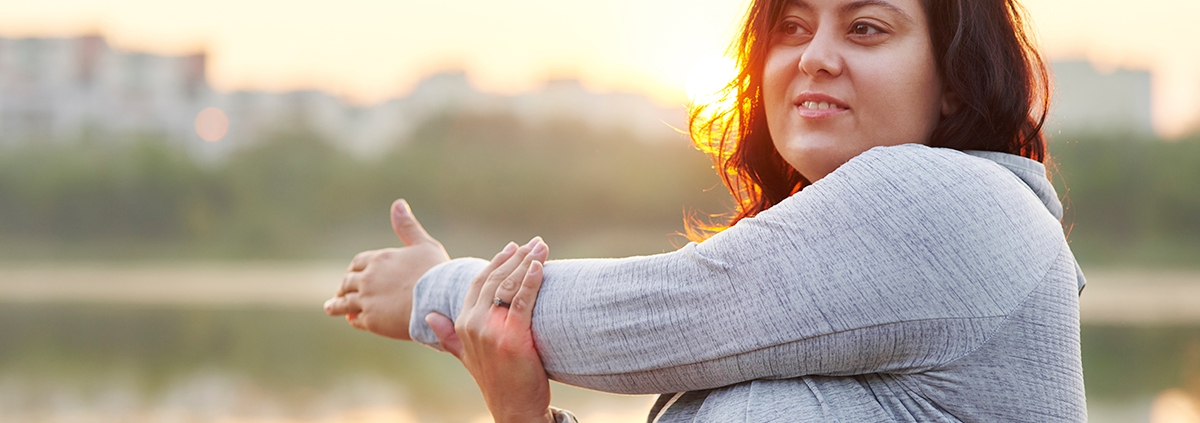 A lady outdoors stretching her left arm.