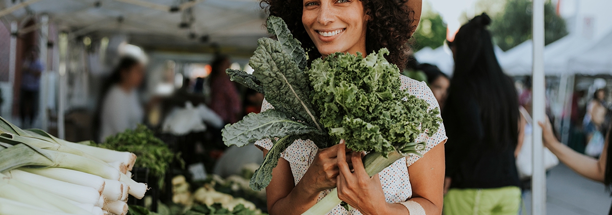 Young lady holding fresh kale leaves at an outdoor market.