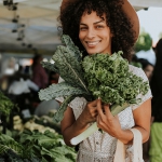 Young lady holding fresh kale leaves at an outdoor market.