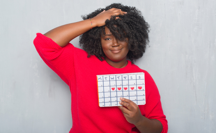 Young african american woman over grey grunge wall holding menstruation calendar.