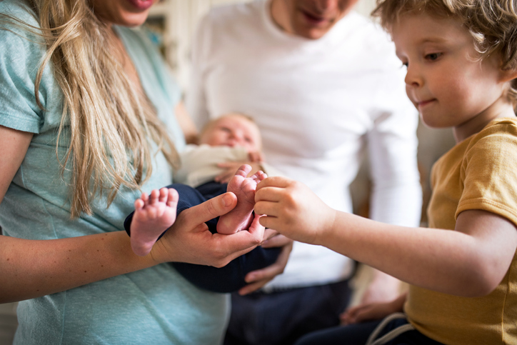 A midsection of parents with a newborn baby and small toddler son at home, worried about the most common birth defects.