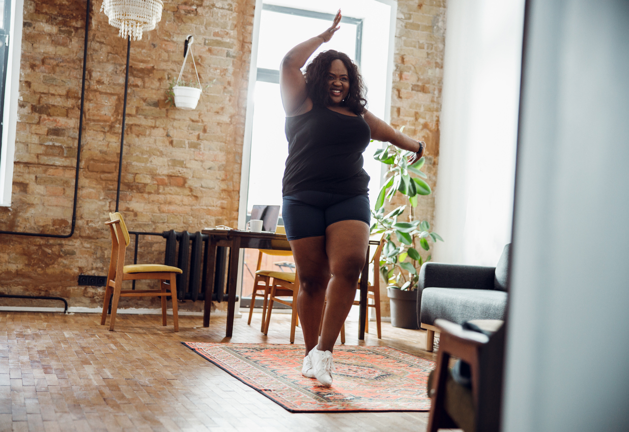 Happy woman with excess weight smiling and dancing alone in sports clothes, knowing Being Active Can Positively Impact Women's Health.