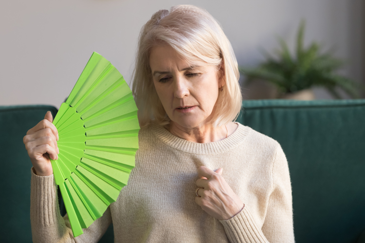 An older woman fanning herself from hot flashes.