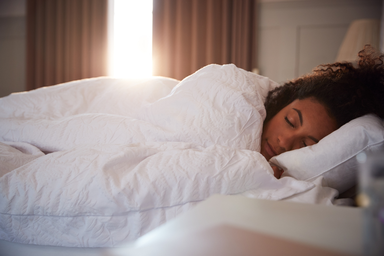 Peaceful Woman Asleep In Bed As Day Break Through Curtains, highlighting the The Importance of Sleep to Women