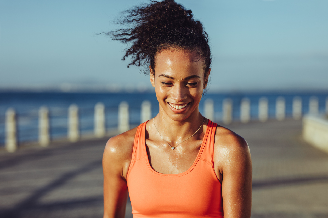 Smiling young female runner taking a breather. Healthy young woman with sweat standing on the promenade after her workout and smiling, wondering about sweating down there.