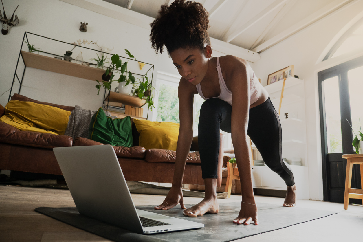 Beautiful young mixed race female exercising at home, online workout on laptop, highlighting balancing staying active for women.