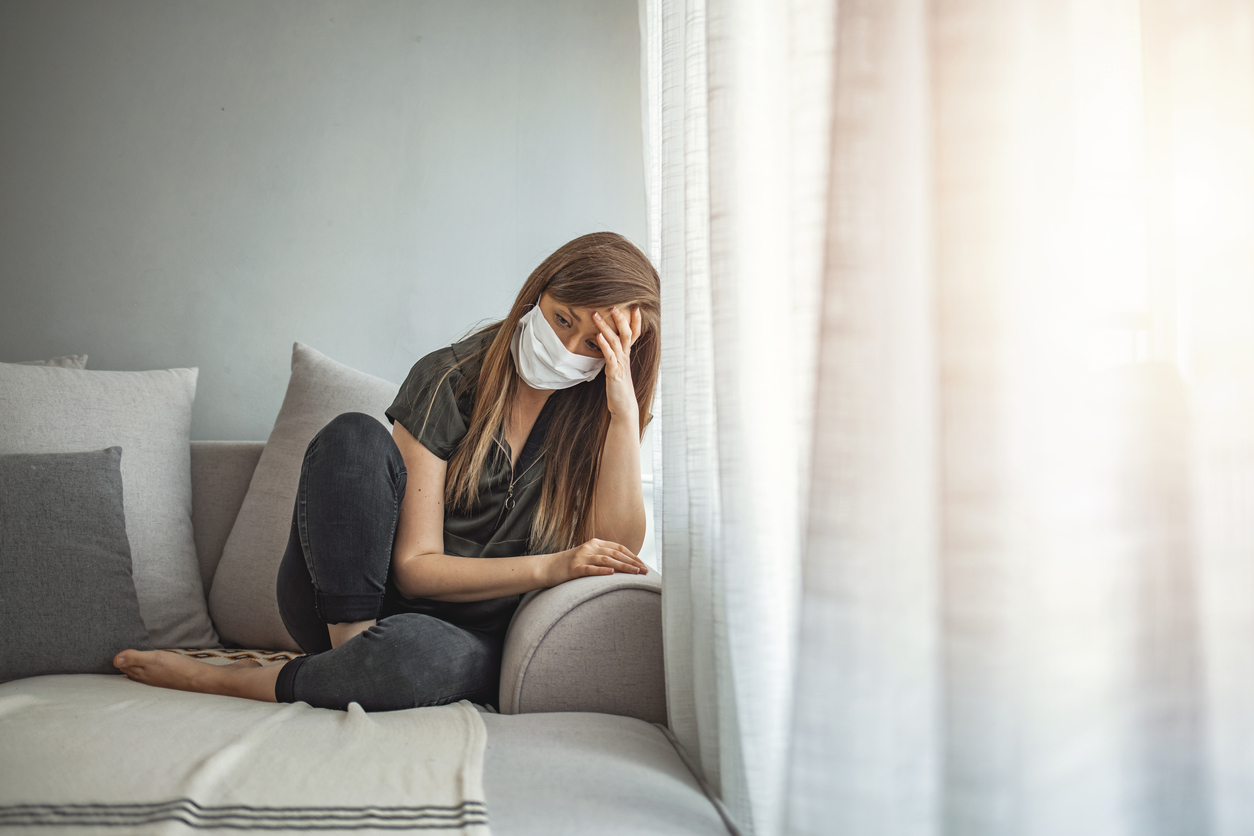 Sad lonely girl isolated stay at home in protective sterile medical mask on face looking at window, highlighting struggling with mental health.