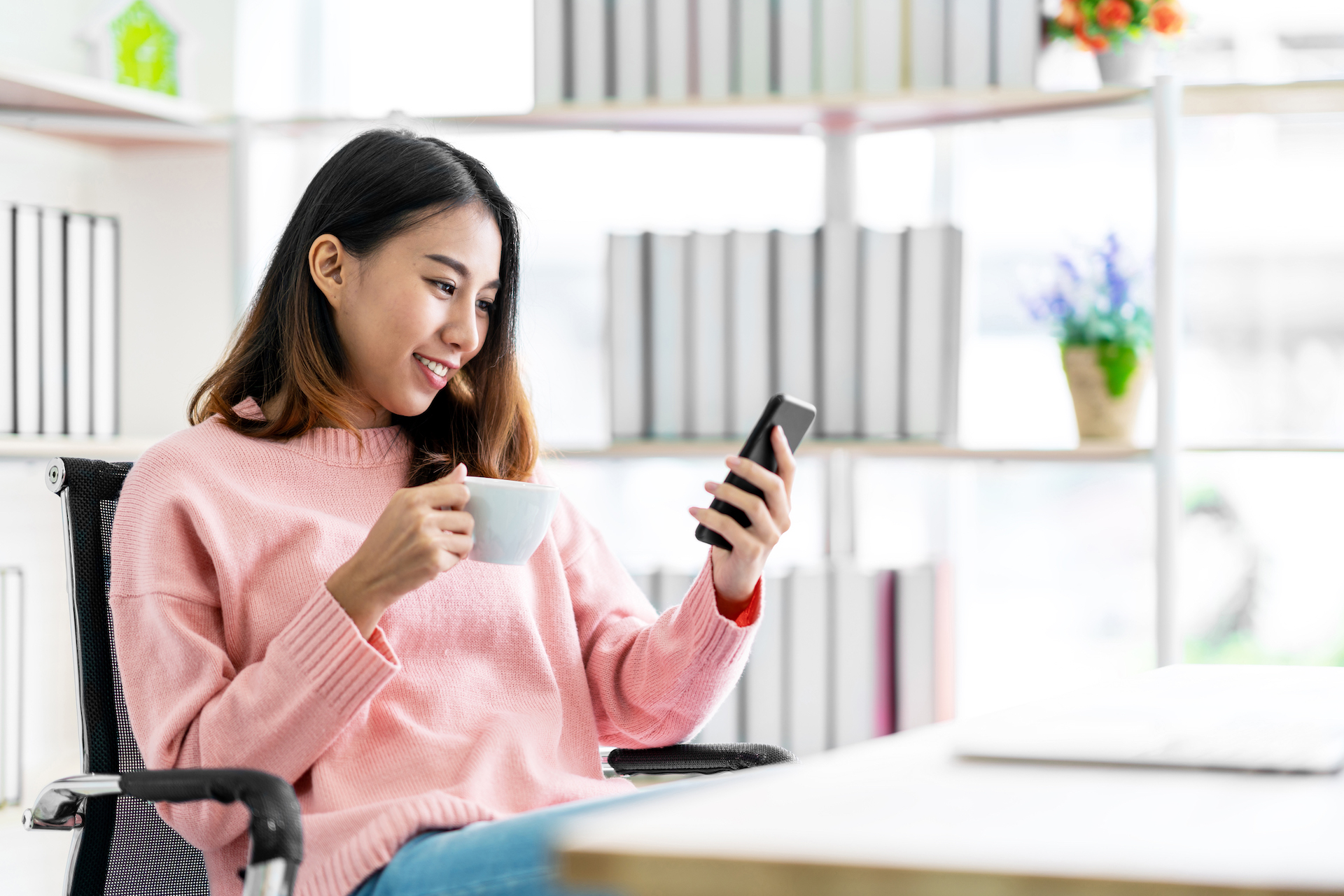 Woman looking at her phone with a cup in hand