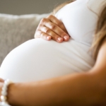 close up of pregnant woman sitting in sofa with hands on her belly