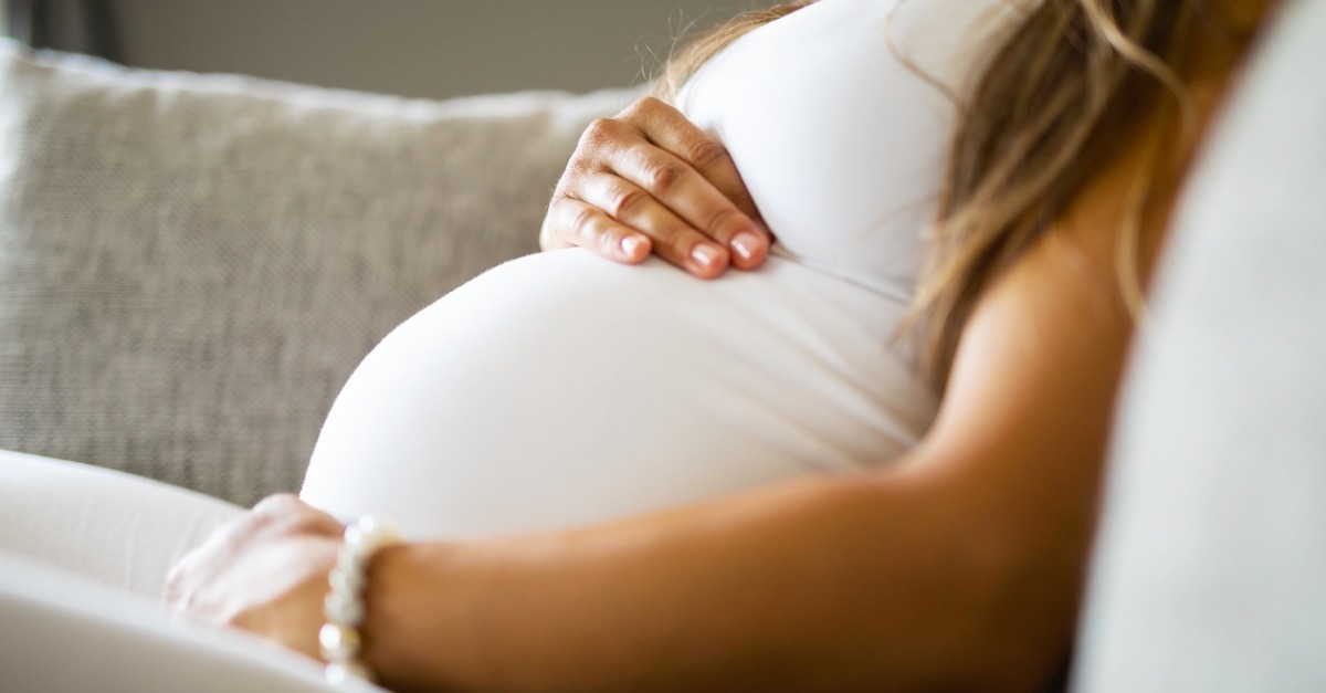 close up of pregnant woman sitting in sofa with hands on her belly