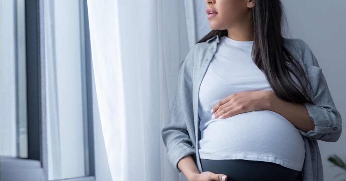 Pregnant woman touching her belly while staring out of a window