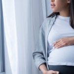 Pregnant woman touching her belly while staring out of a window