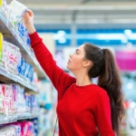 young woman reaching for the top shelf for feminine hygiene products