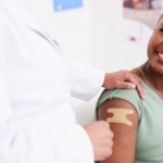 An African American lady smiling after a shot in a medical clinic.