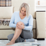 Middle-aged woman at home holding her leg, showing discomfort related to menopause and bone health
