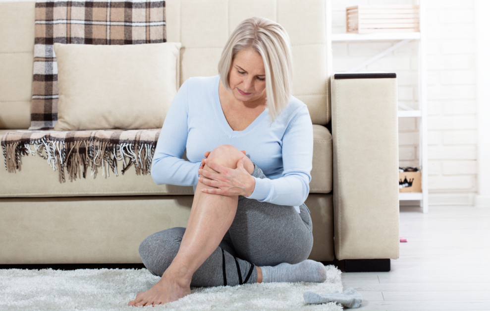 Middle-aged woman at home holding her leg, showing discomfort related to menopause and bone health